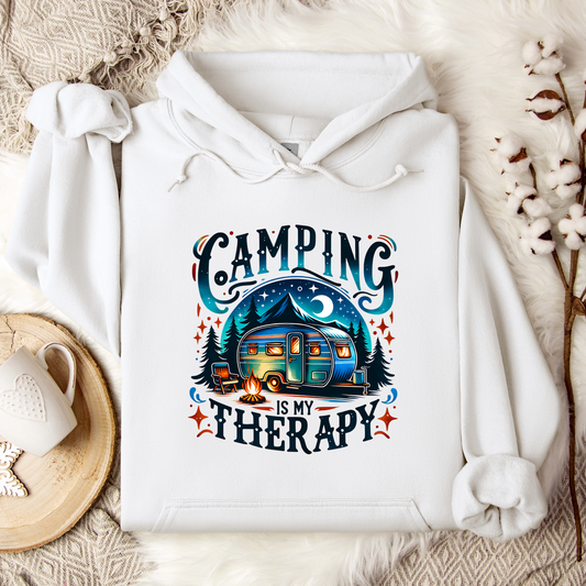 White hooded sweatshirt with 'Camping Is My Therapy' printed on the front, featuring an illustration of a camper, trees, and stars.